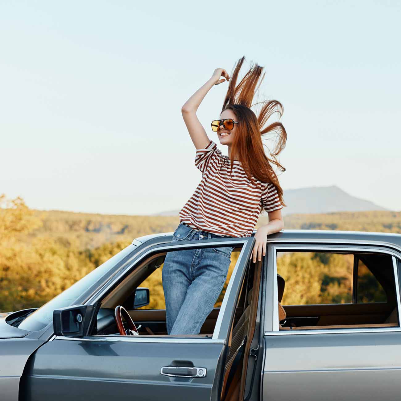 Mujer joven fuera de su auto disfrutando del paisaje