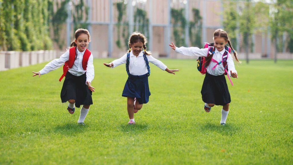 Niños felices corriendo en el césped de la escuela
