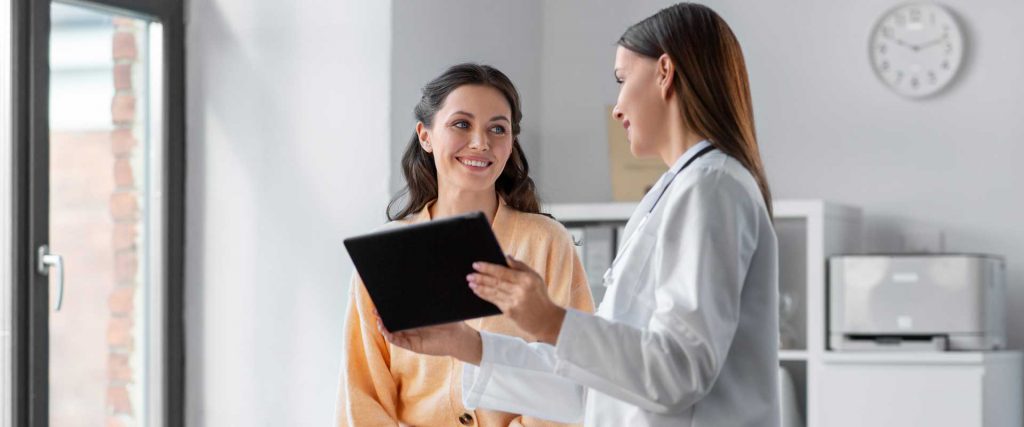 Seguros de Gastos Médicos Mayores: ¿qué son y qué cubren? Doctora mostrándole una tablet a una paciente joven