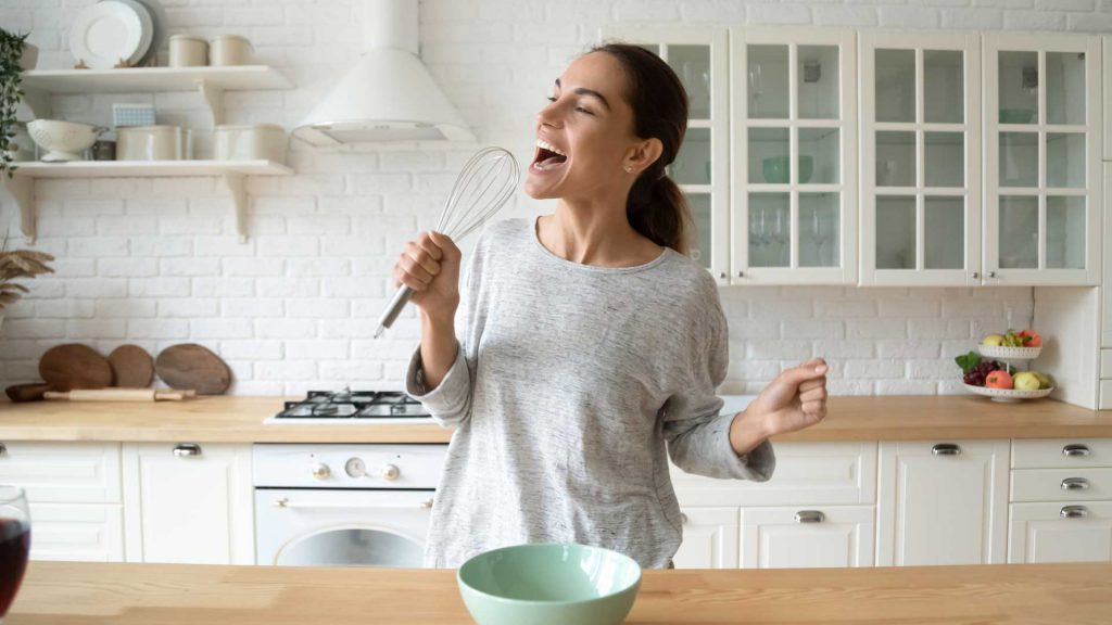 Mujer joven en la cocina cantando con un batidor de mano - HDI SEGUROS