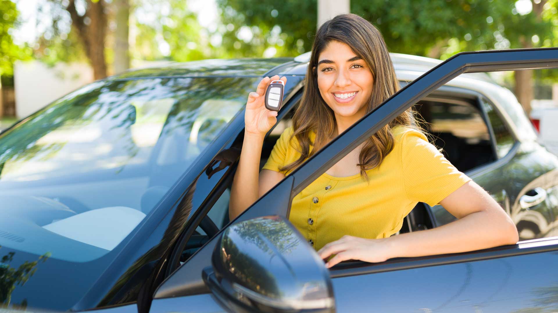 Mujer joven mostrando las llaves de su auto nuevo.