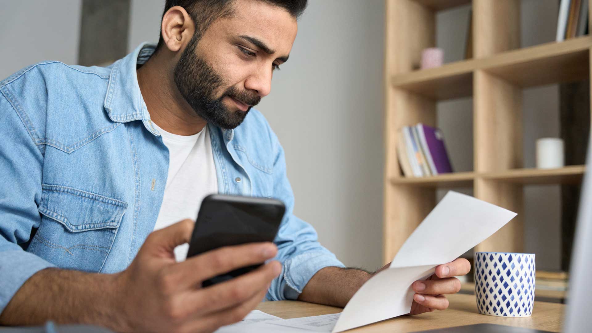 Joven gestionando sus finanzas con su celular y laptop.