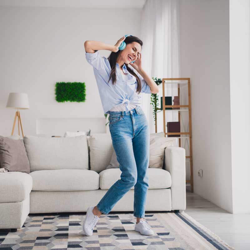 Mujer bailando con audífonos en su casa, en actitud alegre.