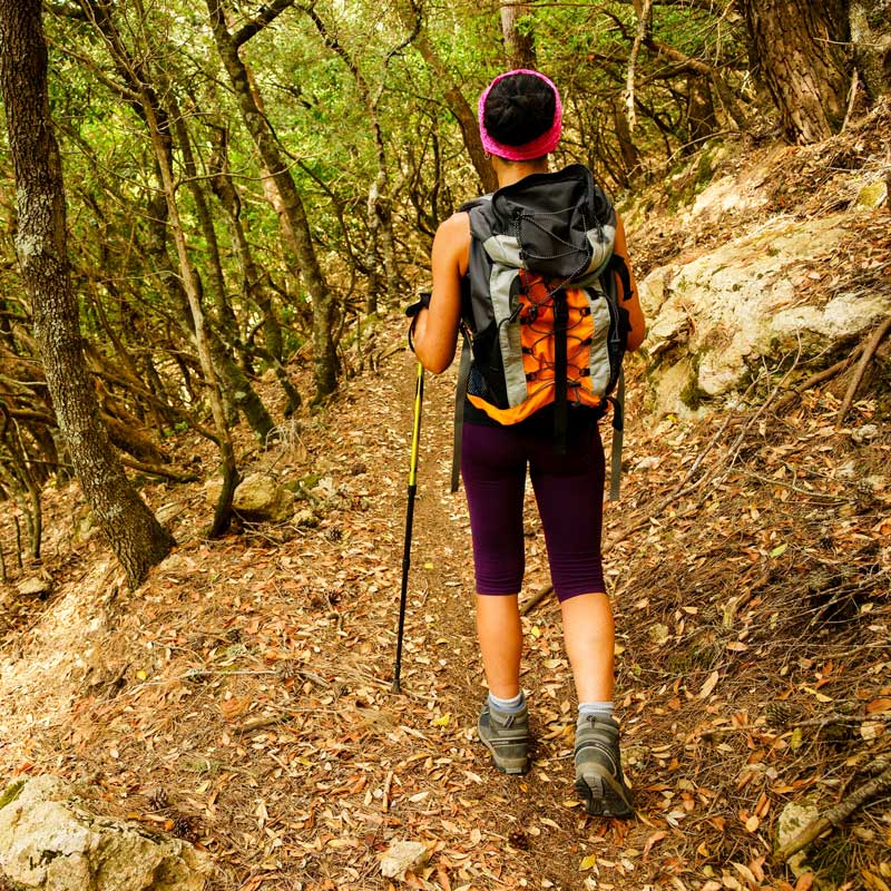 Mujer caminando sola con mochila en un bosque al atardecer.