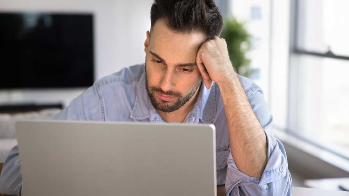 Hombre joven cansado frente a la computadora en su casa.
