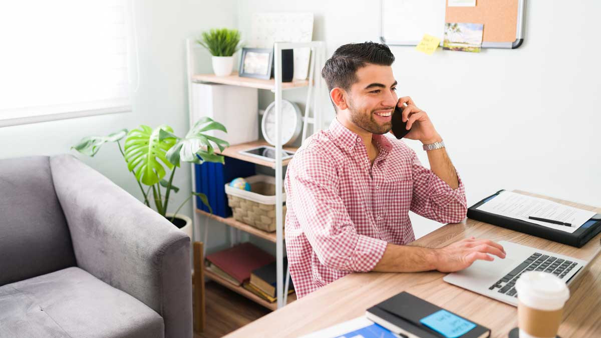 Hombre latino hablando por telefono y trabajando desde su casa.