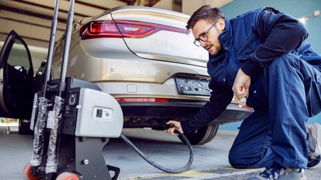 Hombre en taller mecánico con herramientas para medir las emisiones de gas de un auto.