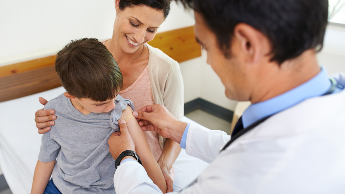 Doctor vacunando a niño sentado junto a su mamá.