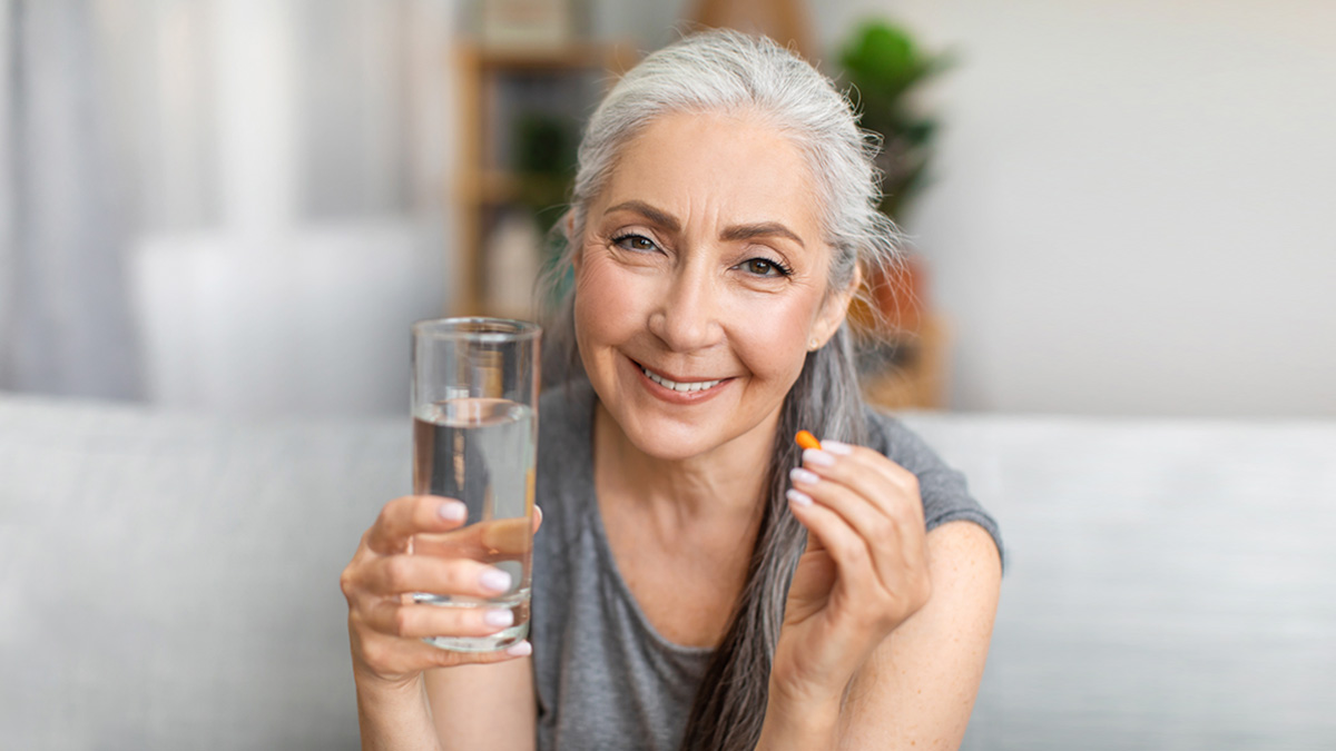 Mujer adulta sonriendo mientras toma un vaso de agua y una pastilla de vitaminas en su casa.