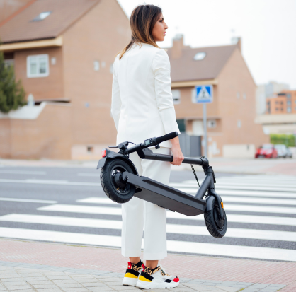 Mujer peaton caminando por la ciudad mientras transporta un scooter eléctrico.