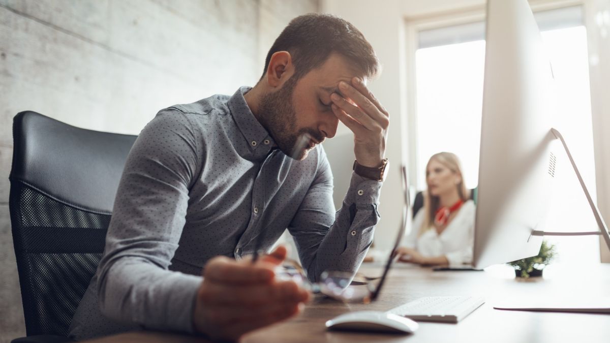 Hombre adulto con dificultades para leer computadora por estrés laboral.