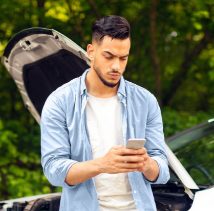 hombre joven llamando a su aseguradora desde el celular junto a su auto accidentado